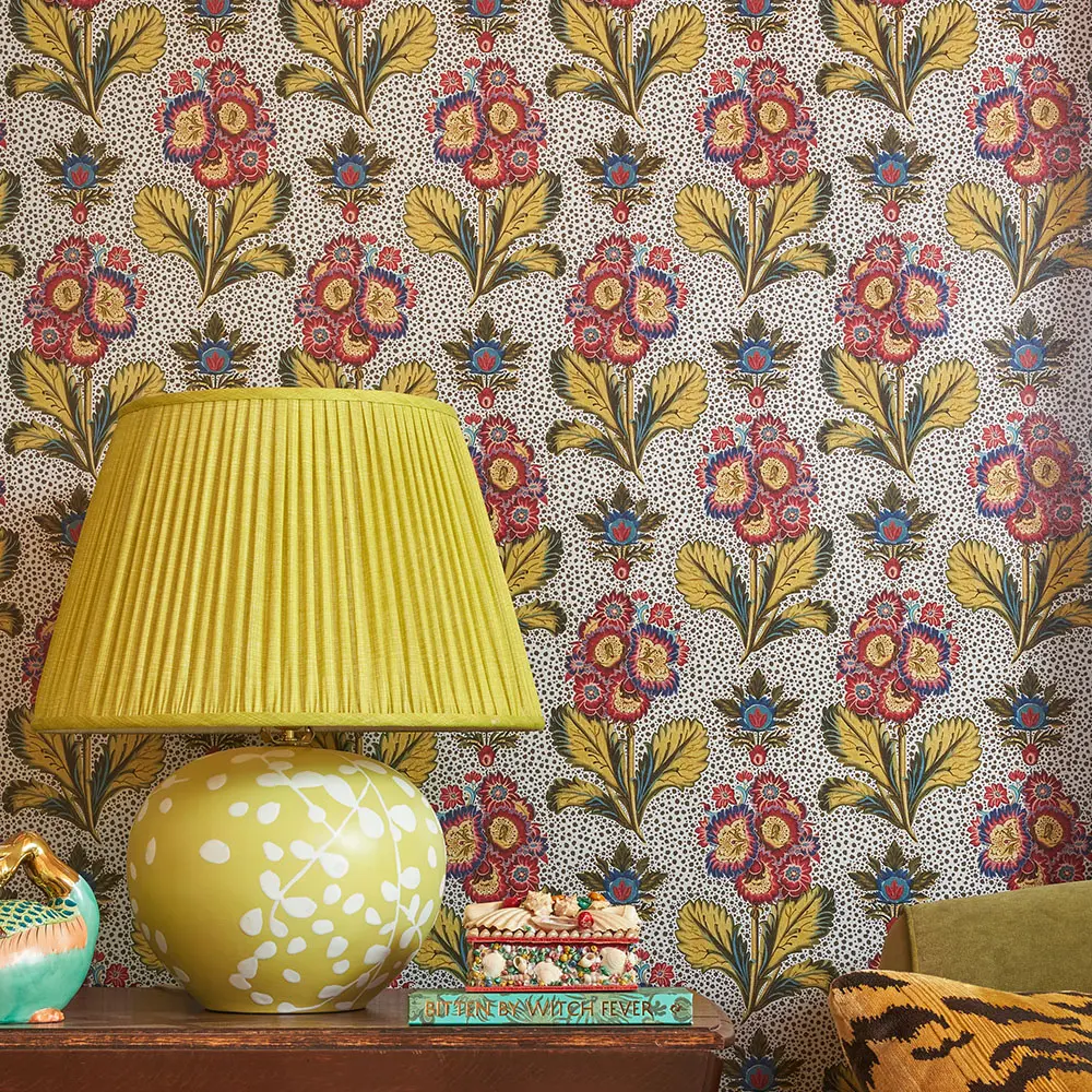 A lamp on a side table behind silver metallic floral wallpaper.