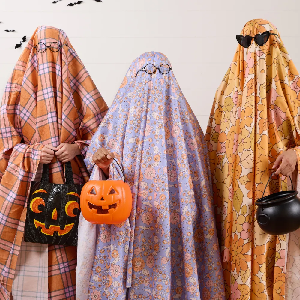 Three people wearing bold floral sheet ghost costumes