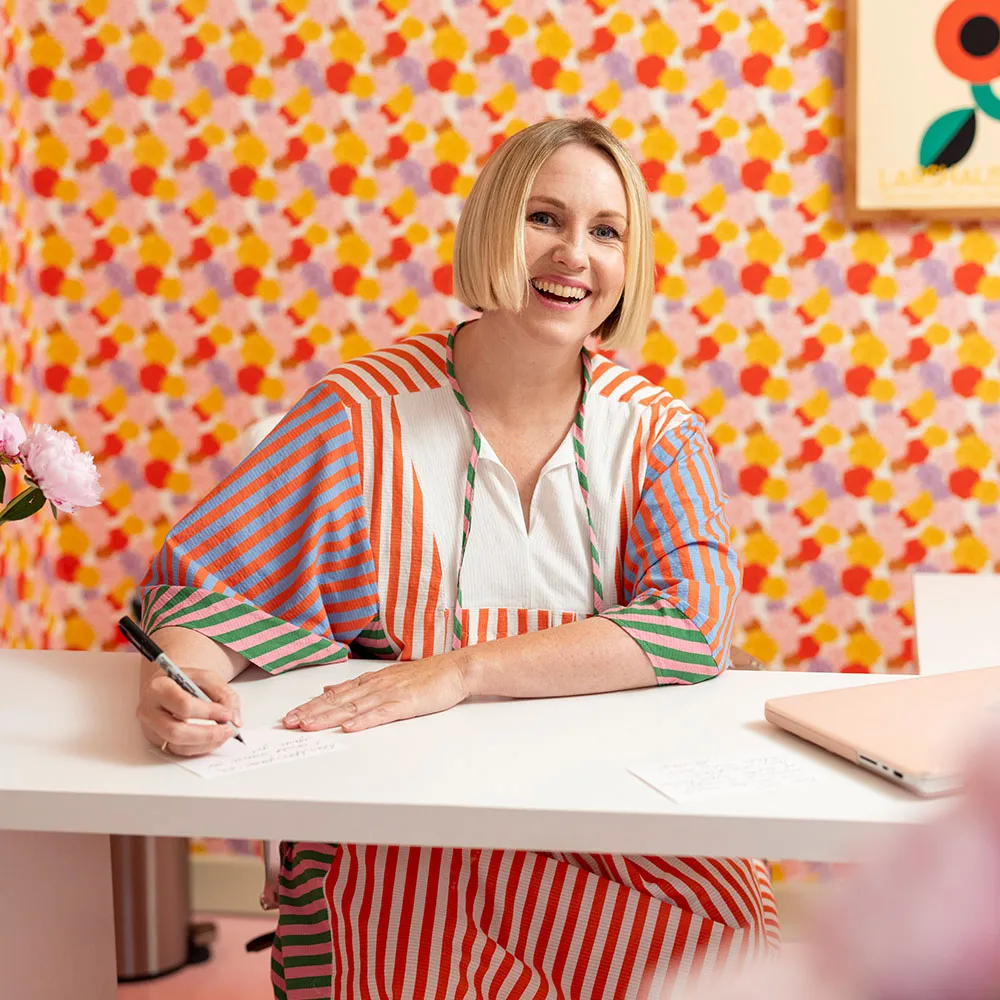 Brittany Watson Jepsen in her craft room behind floral wallpaper.